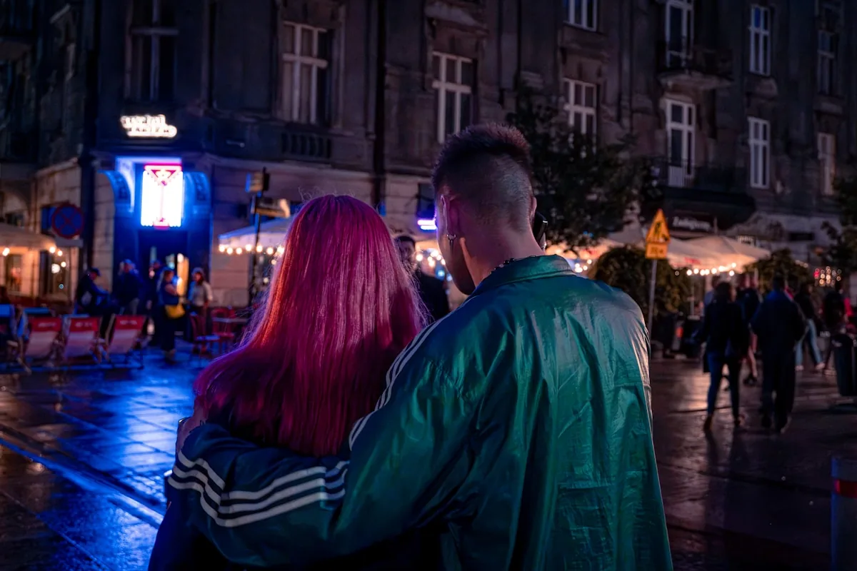A couple walks through a neon-lit city street at night