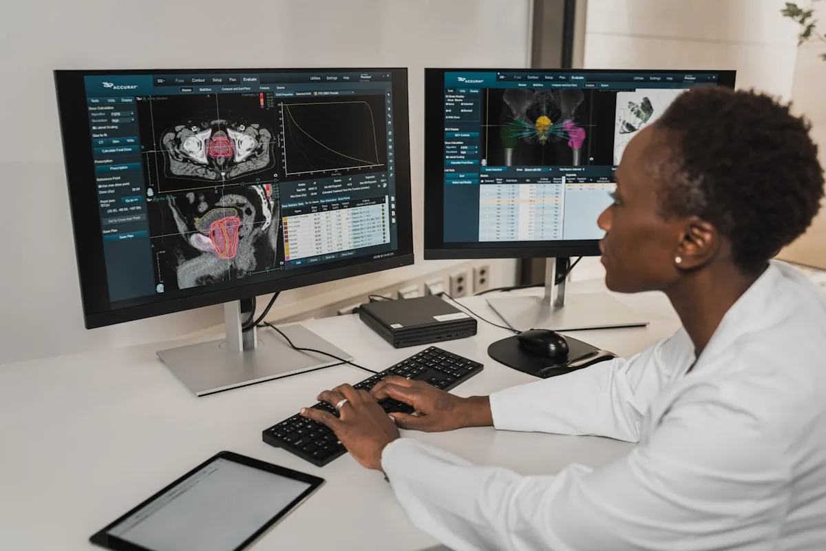 A person in a white coat typing on a keyboard at two medical monitors