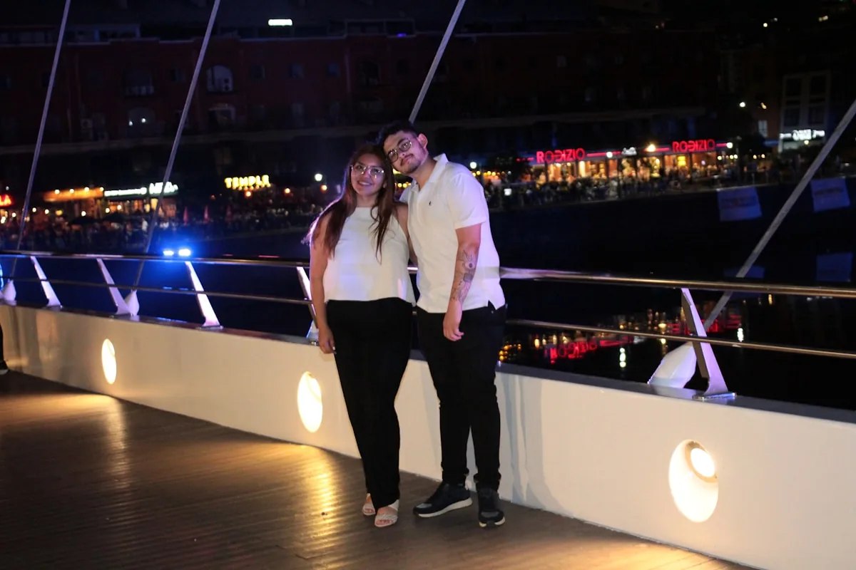 A woman and a man standing on a bridge at night with city lights