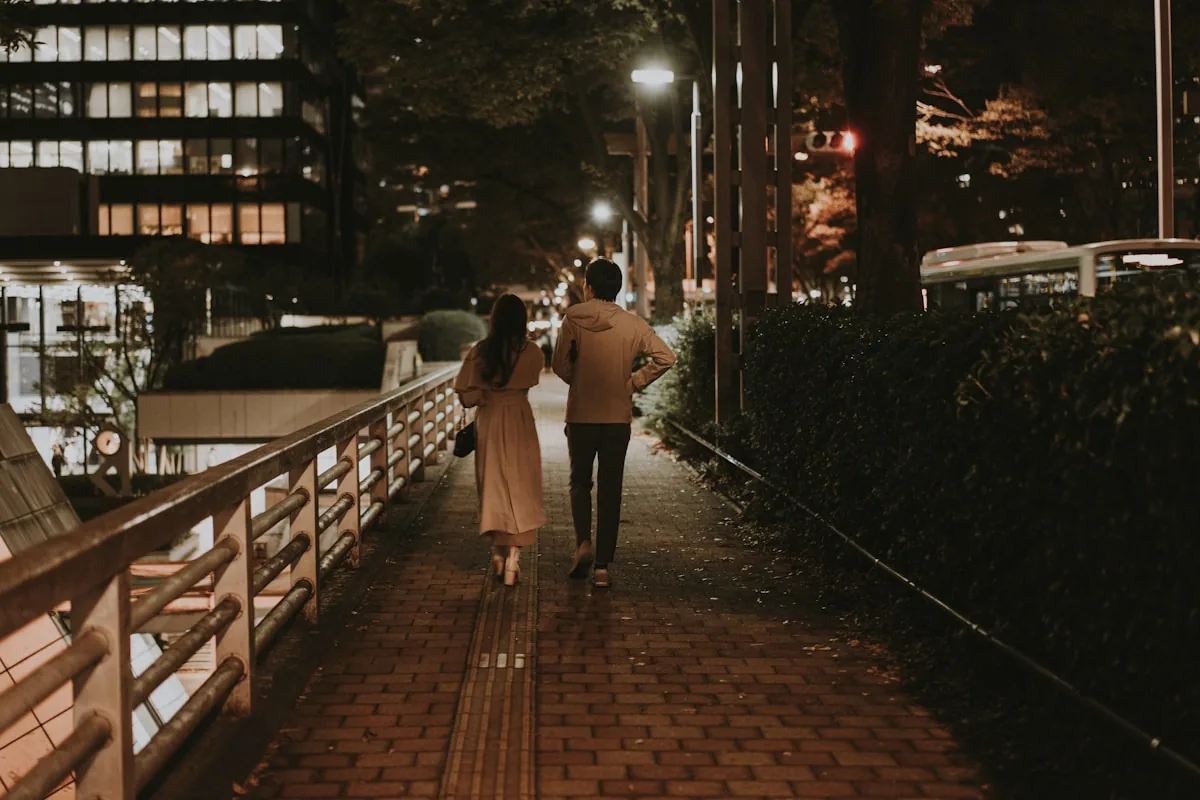 Two people walk on a city sidewalk at night