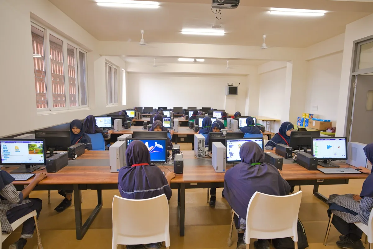Students in hijabs working at computers in a bright school computer lab